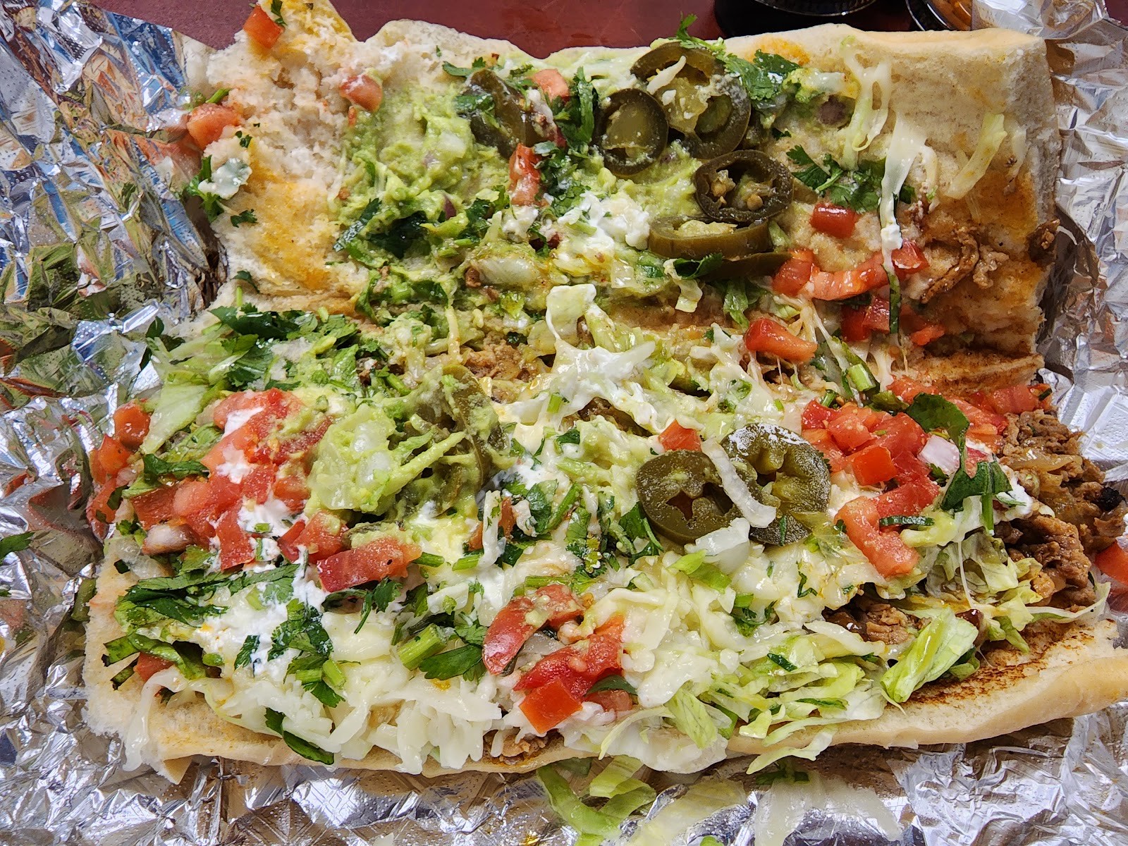 Loaded Mexican-style nachos with guacamole, jalapeños, tomato, lettuce and crema in foil
