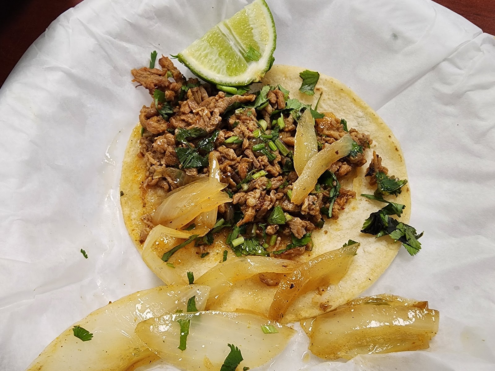 A single carne asada taco with grilled onion, cilantro and a lime wedge on a corn tortilla
