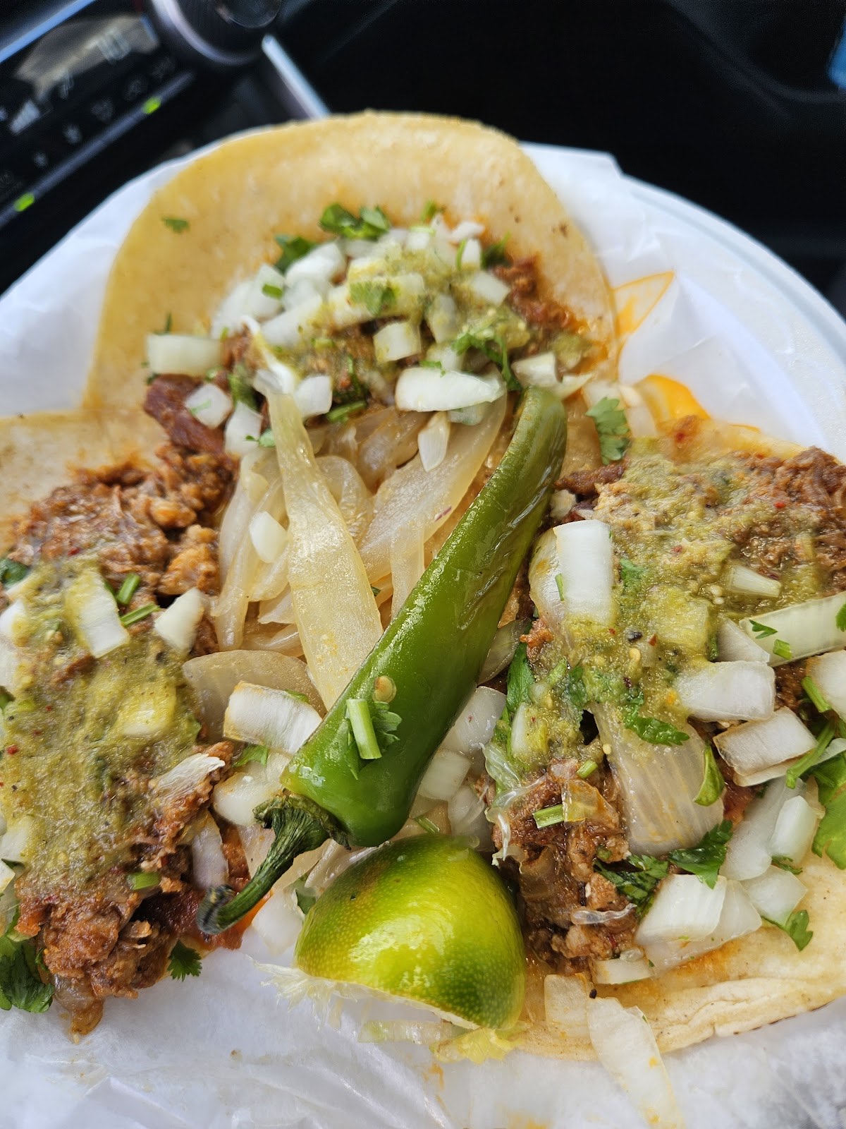Three street tacos al pastor topped with diced onion, cilantro, green salsa, a charred jalapeño and fresh lime
